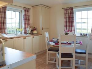 a kitchen with a table and chairs and two windows at Carthouse Cottage in Carew
