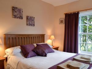 a bedroom with a bed with purple pillows and a window at Lilac Tree Cottage in Dunnington
