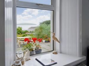 a window with a view of the ocean and flowers at Balcary Mews Cottage in Auchencairn