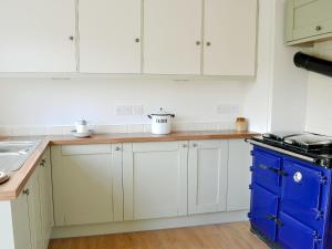 a kitchen with white cabinets and a blue island at Chorlton Moss Cottage in Maer