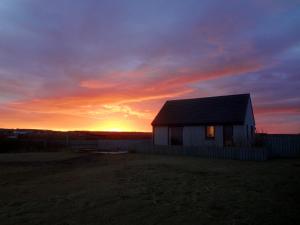 una pequeña casa con una puesta de sol en el fondo en Larachan, en Scarfskerry