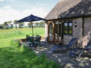 een patio met een tafel en stoelen en een parasol bij The Cowstall in Framfield