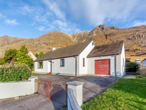 a white house with a red garage in front of mountains at West Home in Torridon