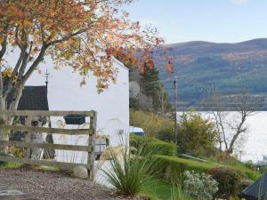 a fence in front of a white building with a lake at Temple House West in Drumnadrochit