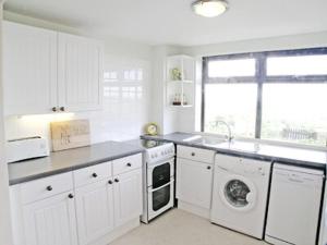 a kitchen with white cabinets and a sink and washing machines at Vale View Cottage in Cinderford