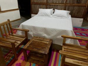 a bedroom with a bed and two wooden chairs at Las Cabañas del Rio in Minca