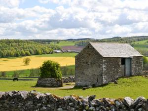 an old stone barn in a field with a stone wall at Mews Cottage in Bampton