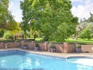 a swimming pool with a brick wall and a tree at Bluebell Cottage - 27635 in Darenth