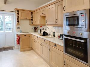 cocina con armarios de madera, fregadero y microondas en The Old Barn en Wansford