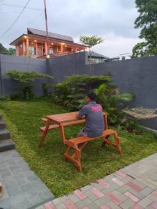 Ein Mann, der auf einem Picknicktisch im Gras sitzt. in der Unterkunft Villa Sky Garden in Bogor
