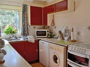 a kitchen with red cabinets and a white dishwasher at Trewithen Farm Bungalow in St Merryn