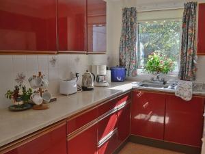 uma cozinha com armários vermelhos, um lavatório e uma janela em Trewithen Farm Bungalow em Saint Merryn