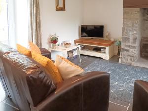 a living room with a leather couch and a television at Honeymead Cottage in Wick