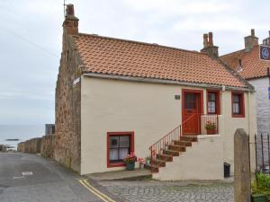 een klein huis met een rode deur en een trap bij Low Tide in Cellardyke