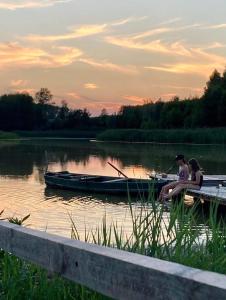 dos personas sentadas en un muelle con un barco en un lago en Agrotourist Maryska Małe Leźno, en Małe Leżno