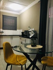 une salle à manger avec une table en verre et des chaises jaunes dans l'établissement Black Rose Guesthouse, à Soweto