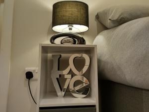a nightstand with a lamp and a sign next to a bed at Queens Holiday Basement in Pembroke Dock