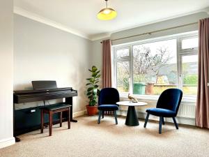 ein Wohnzimmer mit einem Klavier, Stühlen und einem Tisch in der Unterkunft Spacious 3 double bedroomed house in Bicester in Bicester
