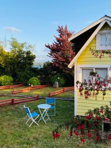 a yellow house with chairs and a table in the yard at La Guapa Hostel in Puerto Varas