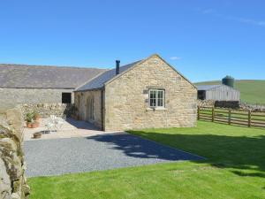 a stone building with a grass yard and a fence at Spindle Well Barn in Elsdon