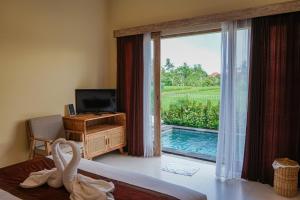 a bedroom with a view of a pool and a television at Kidupa Villa in Ubud