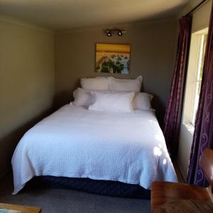 um quarto com uma cama com lençóis brancos e almofadas em Tahakopa Lodge - Cabin em Tahakopa