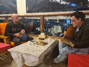 two men sitting at a table with a guitar at Seedi Yousef Hostel & Cafe in Nazareth
