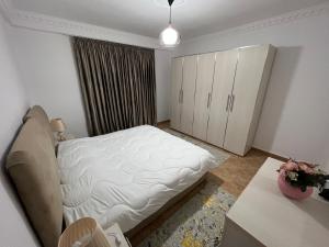 a bedroom with a white bed and a table and cabinets at Daily rent apartment city center Elbasan 6 in Elbasan