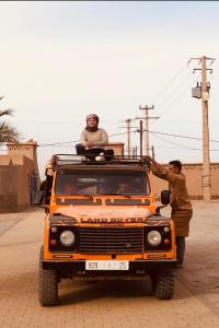 two men standing on the top of an orange truck at Enjoy Moda Camp Merzouga tours- Camel sunset sunrise Quad Sunboarding ATV in Merzouga