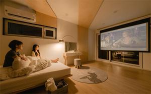 twee personen zittend op een bed in een kamer met een tv bij Tongyeong Amusing Story in Tongyeong