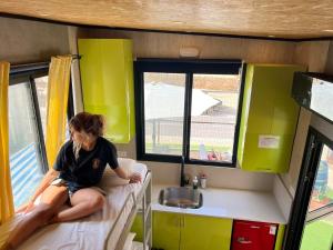 kobieta siedząca na łóżku w małym domku w obiekcie Roger's Hostel Tel Aviv (age 18-45) w Tel Awiwie
