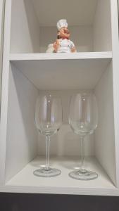 Dois copos de vinho numa prateleira branca com uma estatueta de chef. em Kiviõli Apartment em Kiviõli