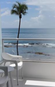 una silla blanca y una palmera en un balcón con vistas al océano en Bahia Flat Apt 107, en Salvador