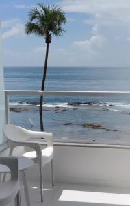 una silla blanca y una palmera en un balcón con vistas al océano en Vista Mar Apt 107, en Salvador