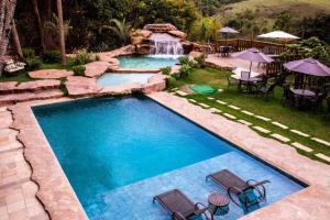 a swimming pool with two chairs and a waterfall at Hotel Fazenda Horizonte Belo in Brumadinho