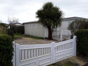 a white fence in front of a house with a palm tree at Le Vert Océan in Talmont