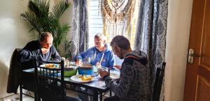 un grupo de tres hombres sentados en una mesa comiendo comida. en Ghar - Homestay, Where Family Lives Together, en Aravankādu