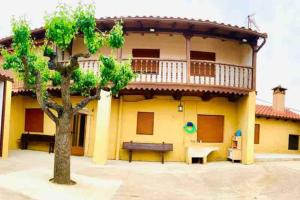 żółty dom z balkonem i drzewem w obiekcie Astorga. León. Piscina. Casa Val de San Lorenzo. w mieście Val de San Lorenzo