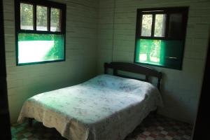 um pequeno quarto com uma cama e 2 janelas em Casa de Campo - Sítio da tia Vera em Maquiné