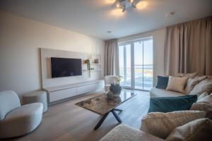 een woonkamer met een bank en een tv bij By Sea, Full Sea View, balcony, use of hotel Pool and Sauna in Cadzand