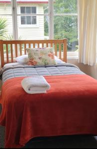 a bed with a red blanket and two towels on it at The Nurses Home Guesthouse - Reefton in Reefton