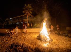 personas de pie alrededor de un fuego en la playa por la noche en Cocodimama Resort Hotel Room en James Cistern