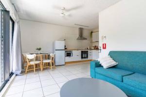 a living room with a blue couch and a kitchen at Little Coastal Haven apartment with a pool! in Cannonvale