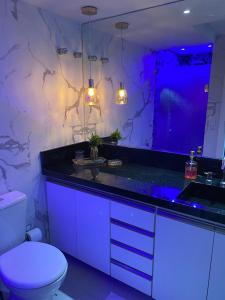 baño con aseo y lavabo con iluminación púrpura en Belo apartamento Ondina Apart, en Salvador