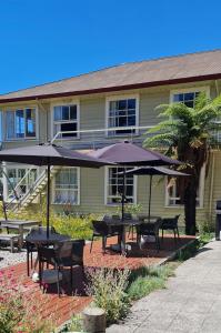 un patio con mesas y sombrillas frente a un edificio en The Nurses Home Guesthouse - Reefton, en Reefton