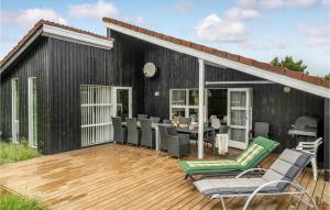 a black house with a deck with chairs and a table at Amazing Home In Ringkbing With 5 Bedrooms, Sauna And Wifi in Klegod