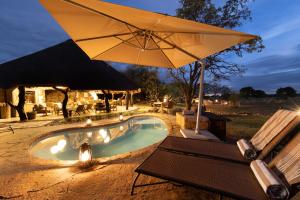 a swimming pool with an umbrella and a table at Kwafubesi Tented Safari Camp in Mabula