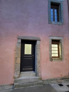 a pink building with a black door and two windows at maison des vendangeurs in Villarzel-Cabardès