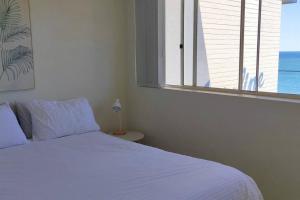 1 dormitorio con cama blanca y ventana en Perched above the waves at Kings Beach apartment, en Caloundra