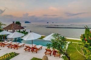 une piscine avec chaises et parasols et l'océan dans l'établissement Villa Oceana, Candidasa, à Candidasa